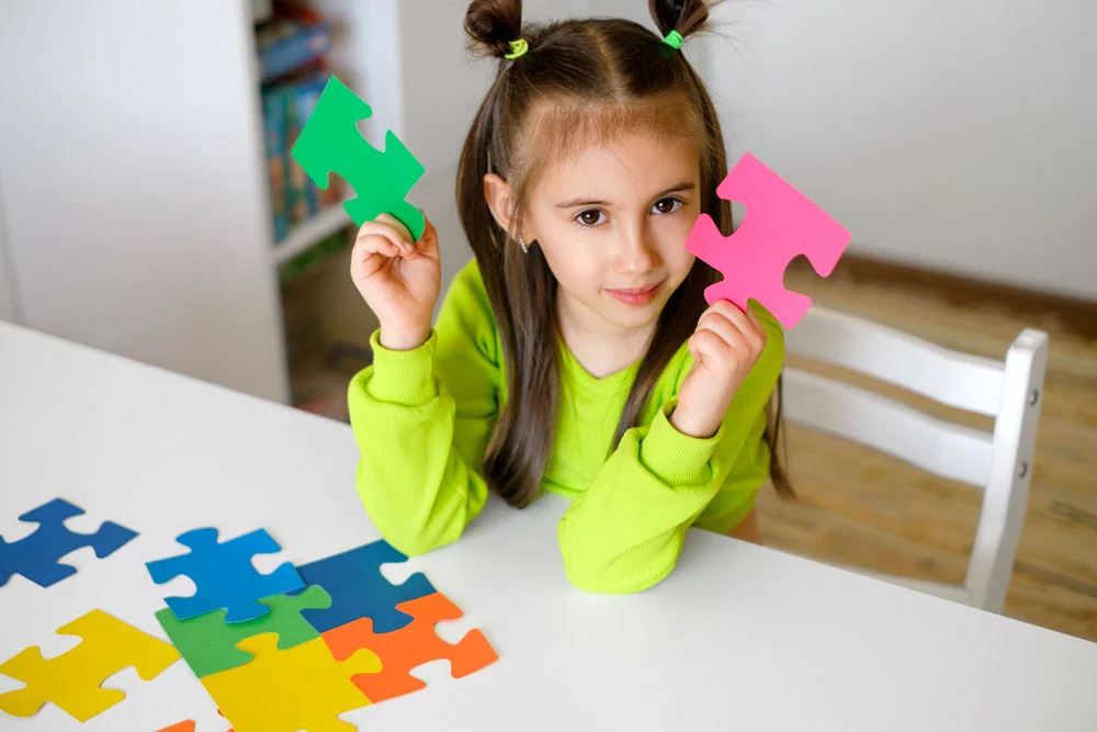 An autistic girl sitting at a table, focused on assembling a puzzle at the Collaboration Station Autism Center. Her hands carefully piece together the puzzle, reflecting concentration and engagement in the therapeutic aba therapy activity